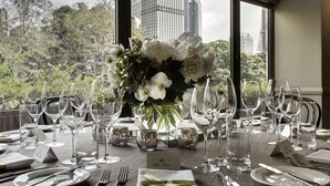 A table set for a meal with a view of a cityscape through large windows. - Pullman Sydney Hyde Park (Darlinghurst)