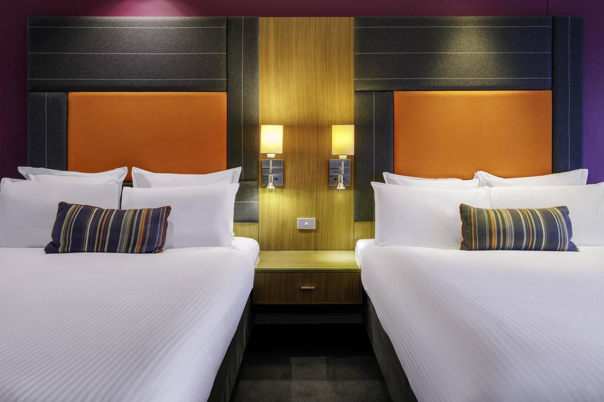 Een hotelkamer met twee bedden, een houten hoofdbord en een nachtkastje met een lamp.