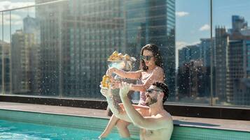 Une piscine avec vue sur la ville, une balustrade en verre et une personne tenant un verre.