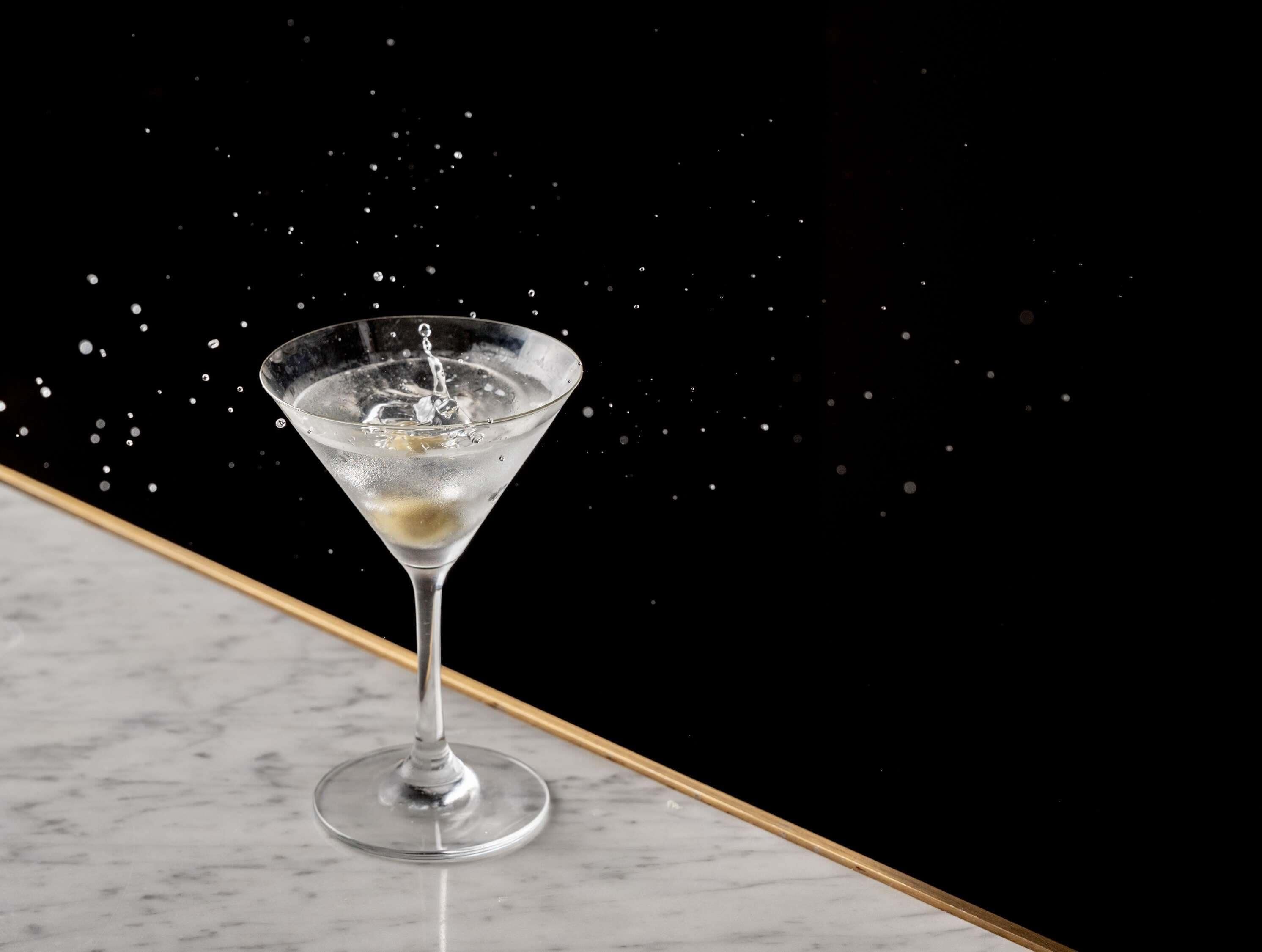 A martini glass on a marble surface with a dark background.