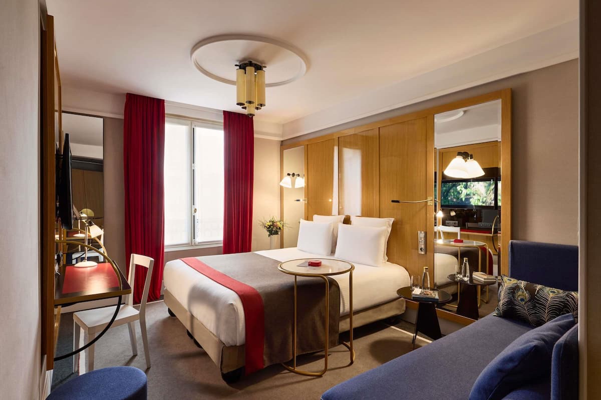 A hotel room with a bed, a desk, a chair, a sofa, a TV, and a mirror.