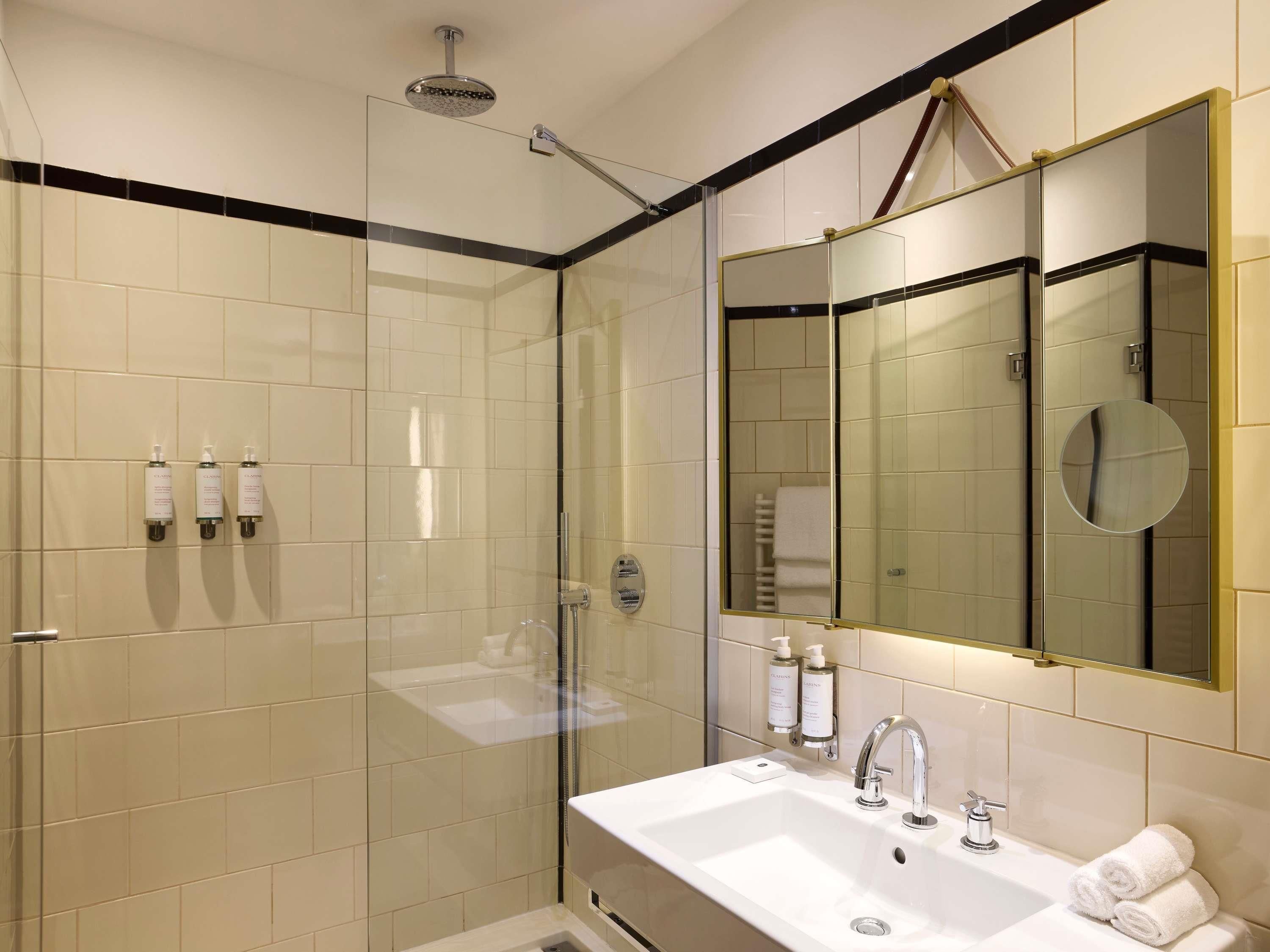 A modern bathroom with a glass-enclosed shower, a sink with a mirror, and toiletries on the wall.