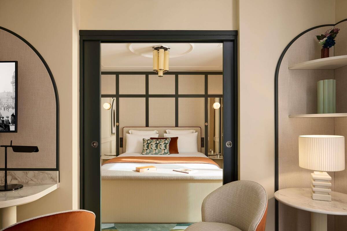 A hotel room with a bed, a chair, a desk, and a lamp.