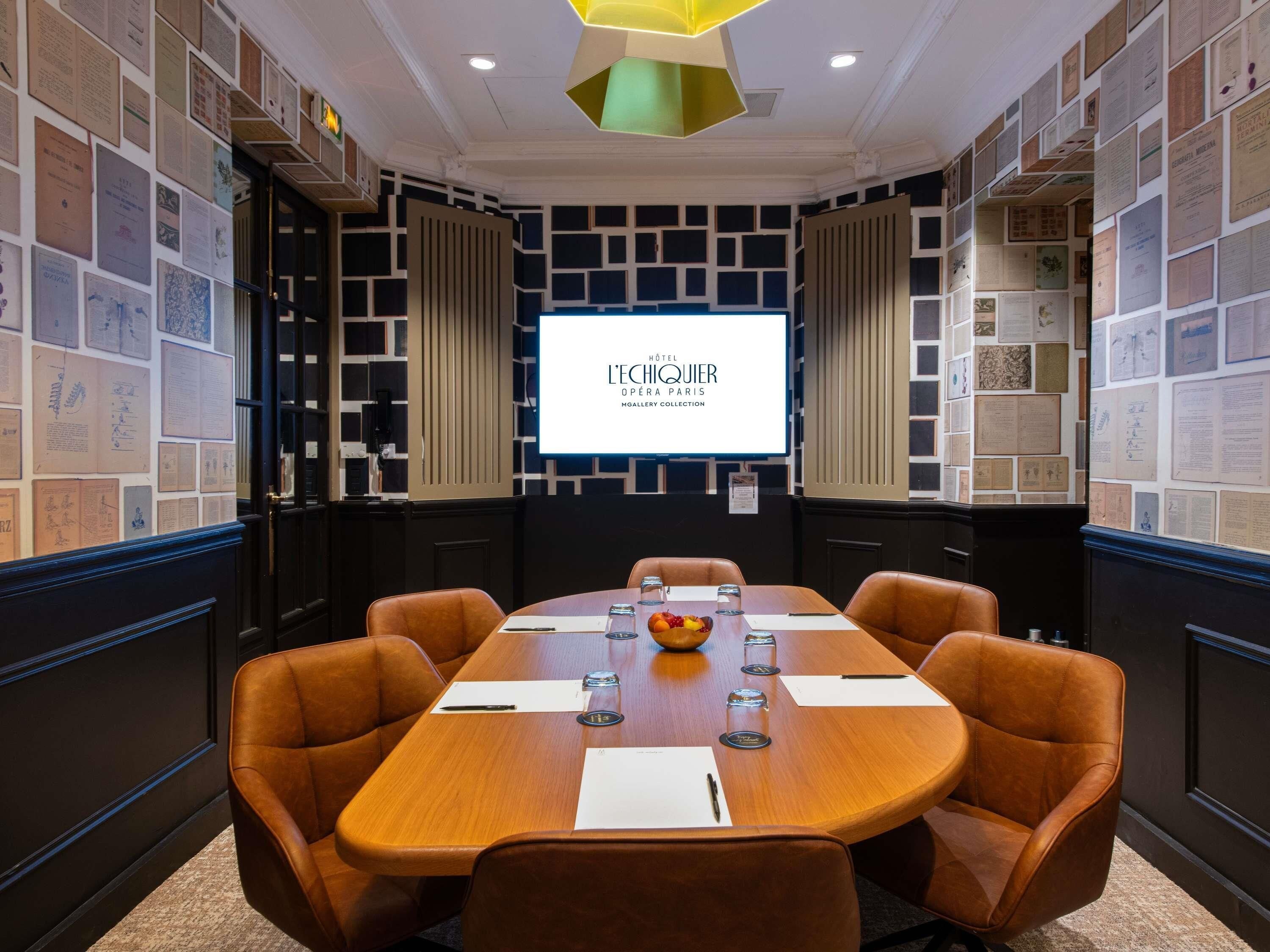 Un salón de conferencias con una mesa grande, sillas de cuero y una pantalla que muestra 'Hôtel L'ÉCHICQUIER O PÉRA PARIS'.