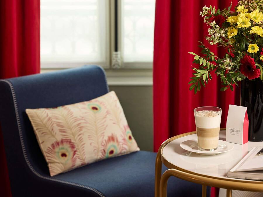 A room with a blue sofa, a white table with a glass of coffee, a vase with yellow flowers, and a red curtain.