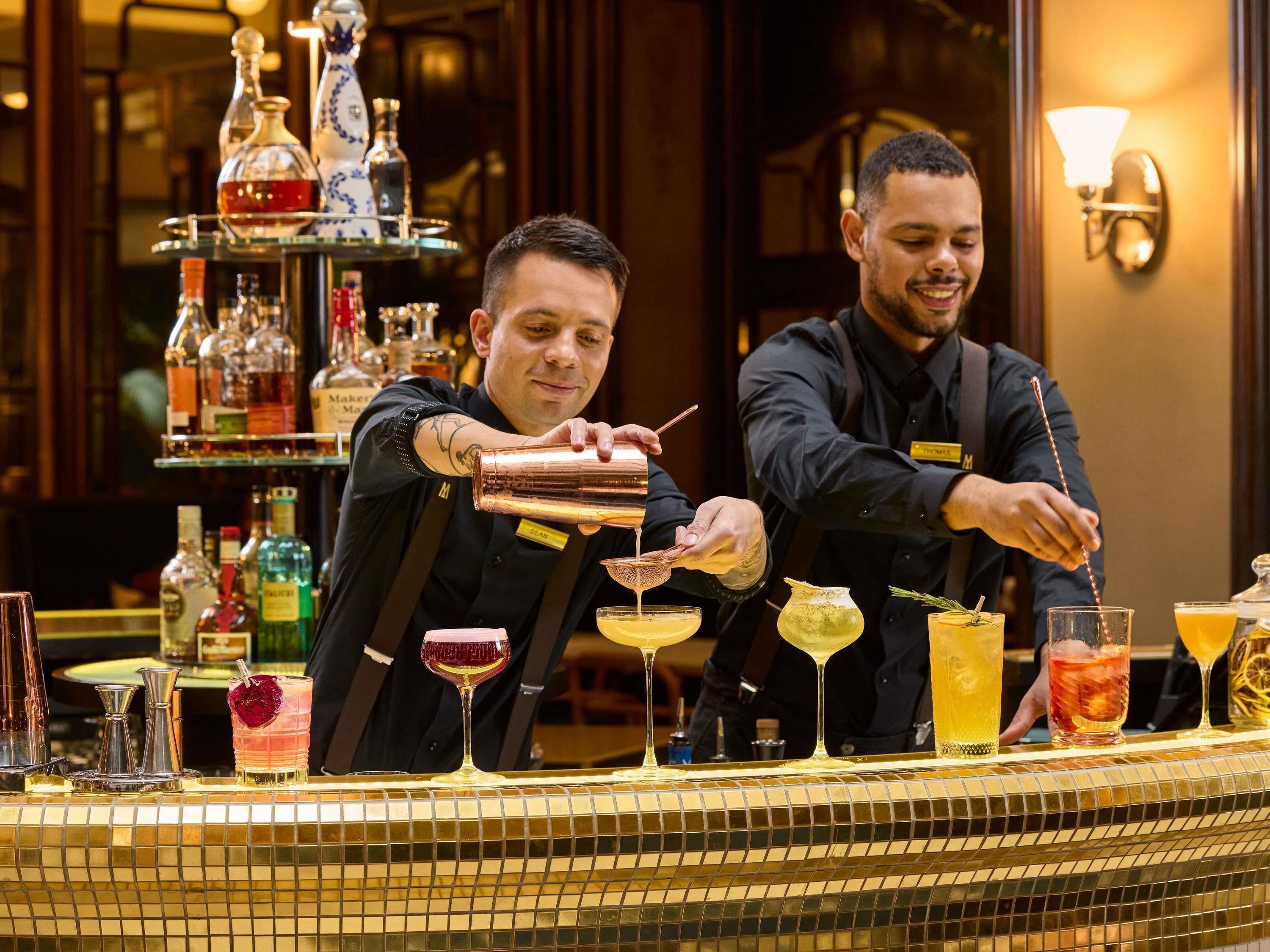 Bartendere laver cocktails bag en bar fyldt med flasker og glas.
