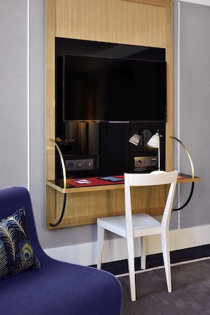 A compact workspace with a wooden desk, a white chair, and a flat-screen TV. - l'Echiquier Opéra Hotel Paris - MGallery Collection (Paris)