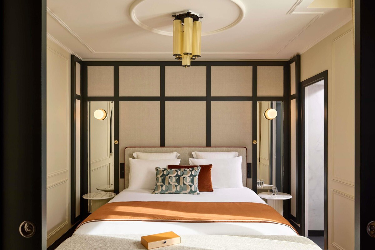 A hotel room with a large bed, a bedside table, a nightstand, a mirror, and a ceiling light fixture.