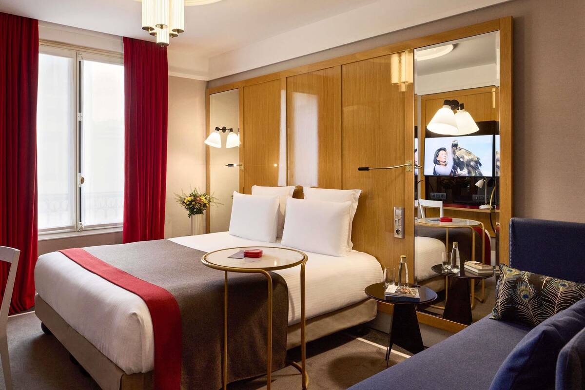 A hotel room with a large bed, a TV, a small table, and a sofa.