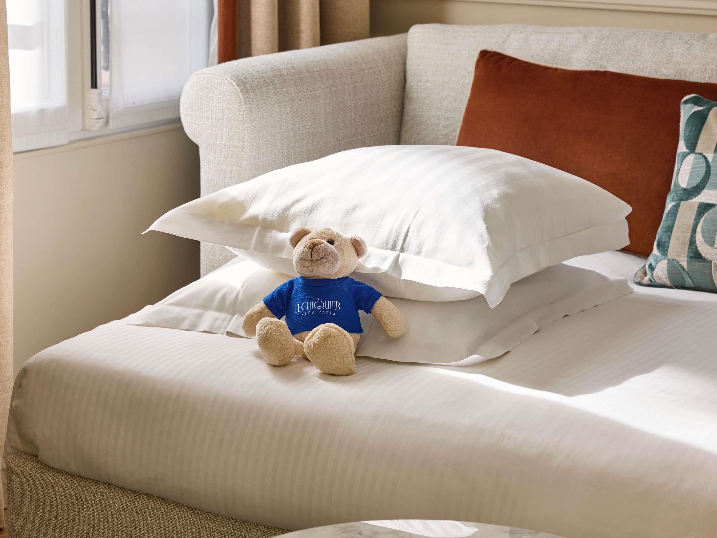 Uma cama com um bicho de pelúcia, um travesseiro e uma almofada.