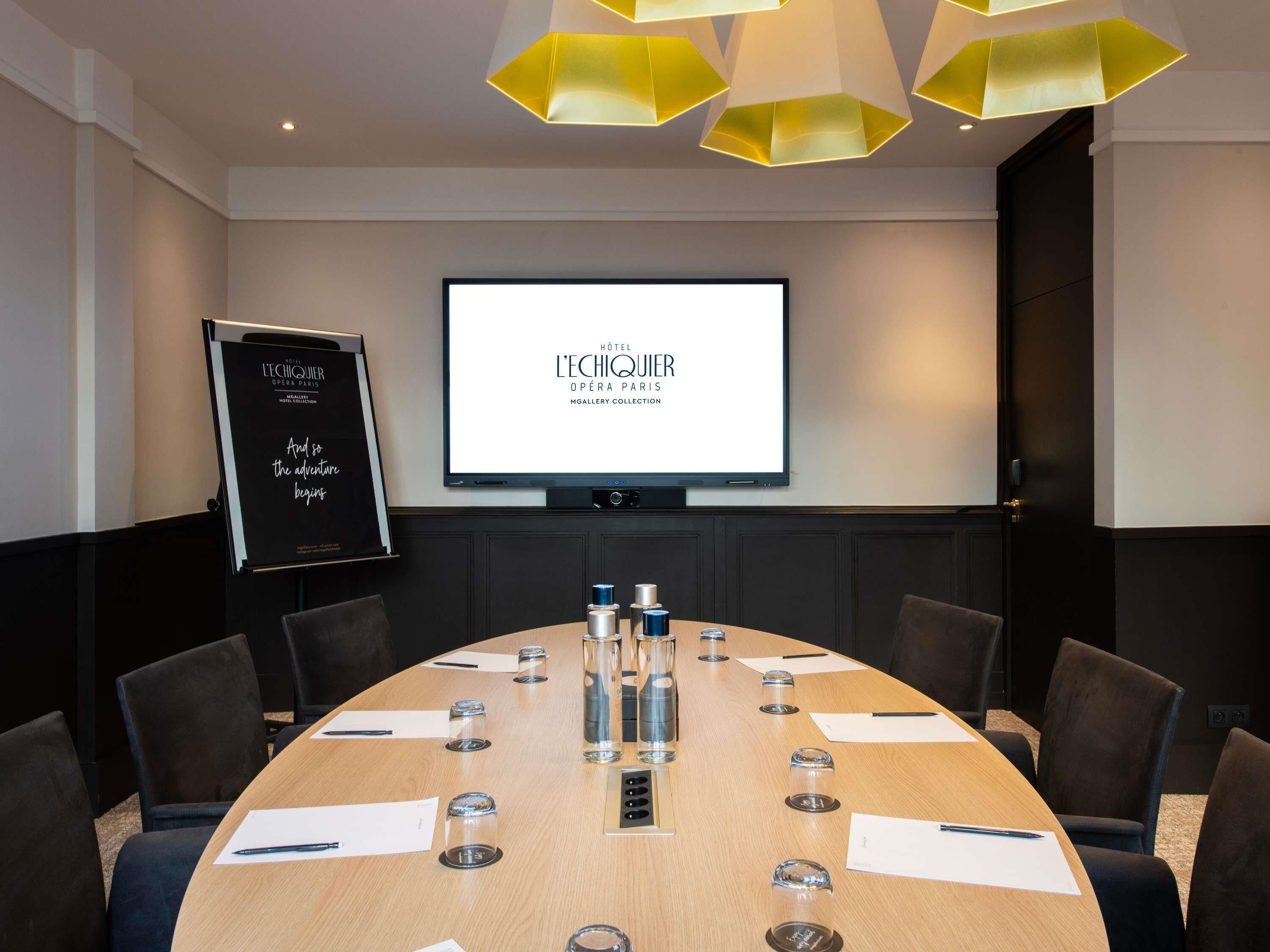 A conference room with a large oval table, chairs, a projector screen, and a whiteboard.