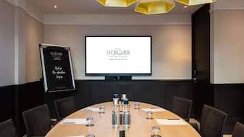 A conference room with a large oval table, chairs, a projector screen, and a whiteboard.