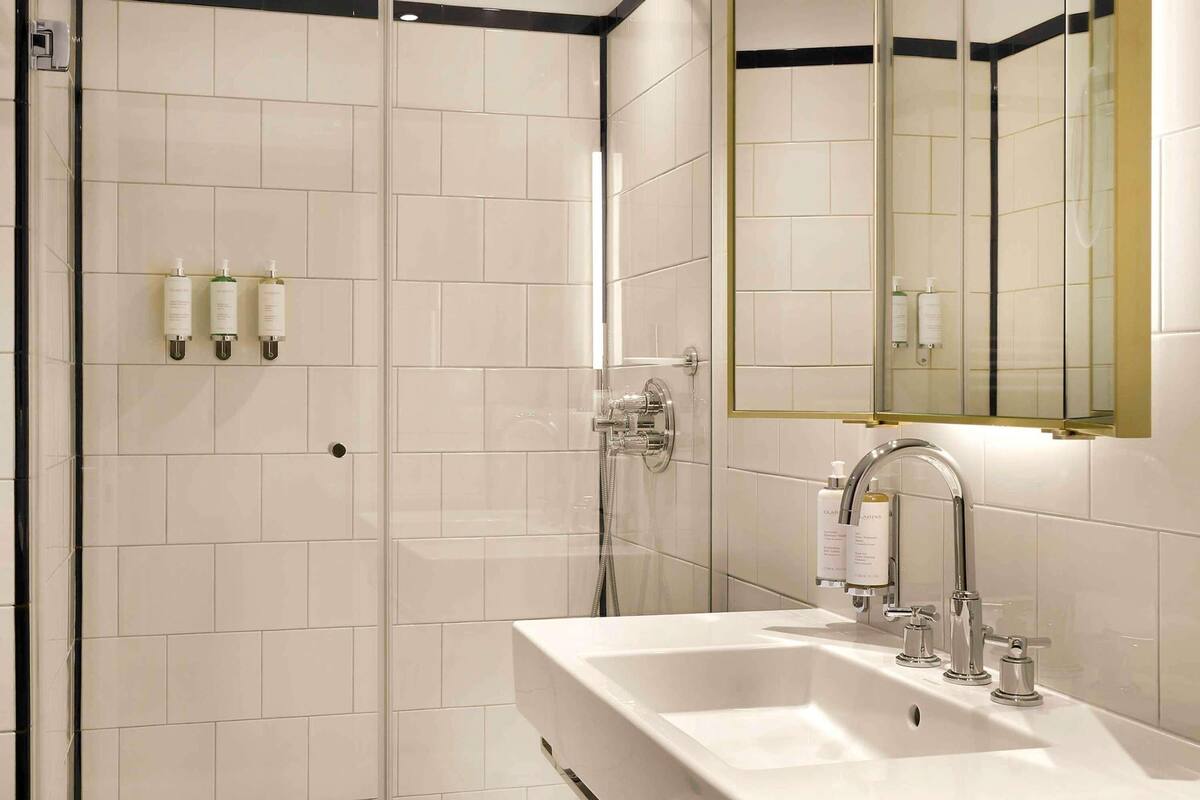 A modern bathroom with a glass-enclosed shower, a large sink with a mirror, and toiletries on the wall.