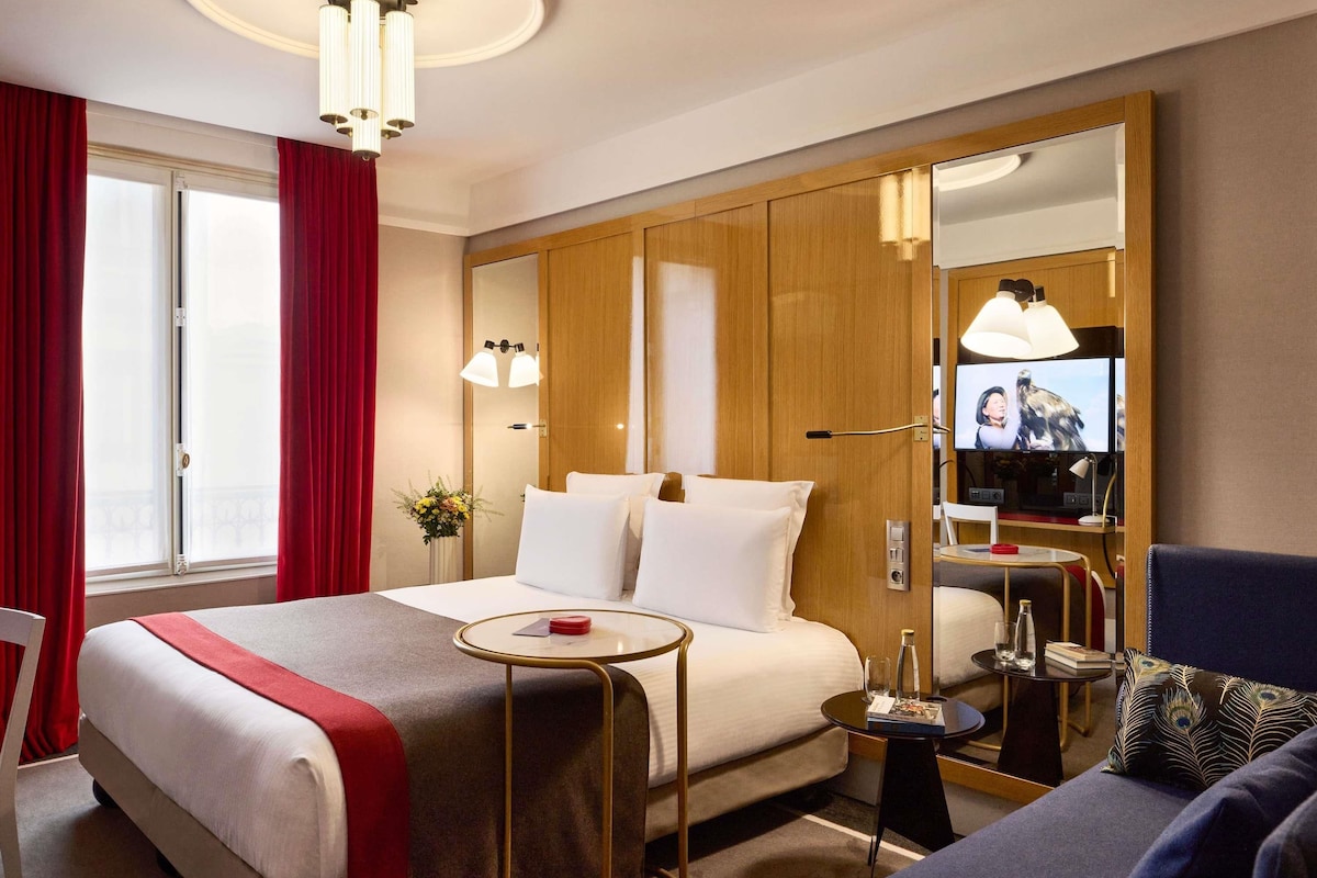 A hotel room with a large bed, a TV, a small table, and a sofa.