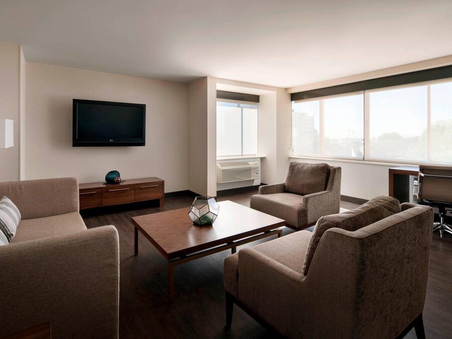 Una sala de estar moderna con un televisor de pantalla plana, asientos cómodos, una mesa de centro y ventanas amplias que ofrecen una vista.