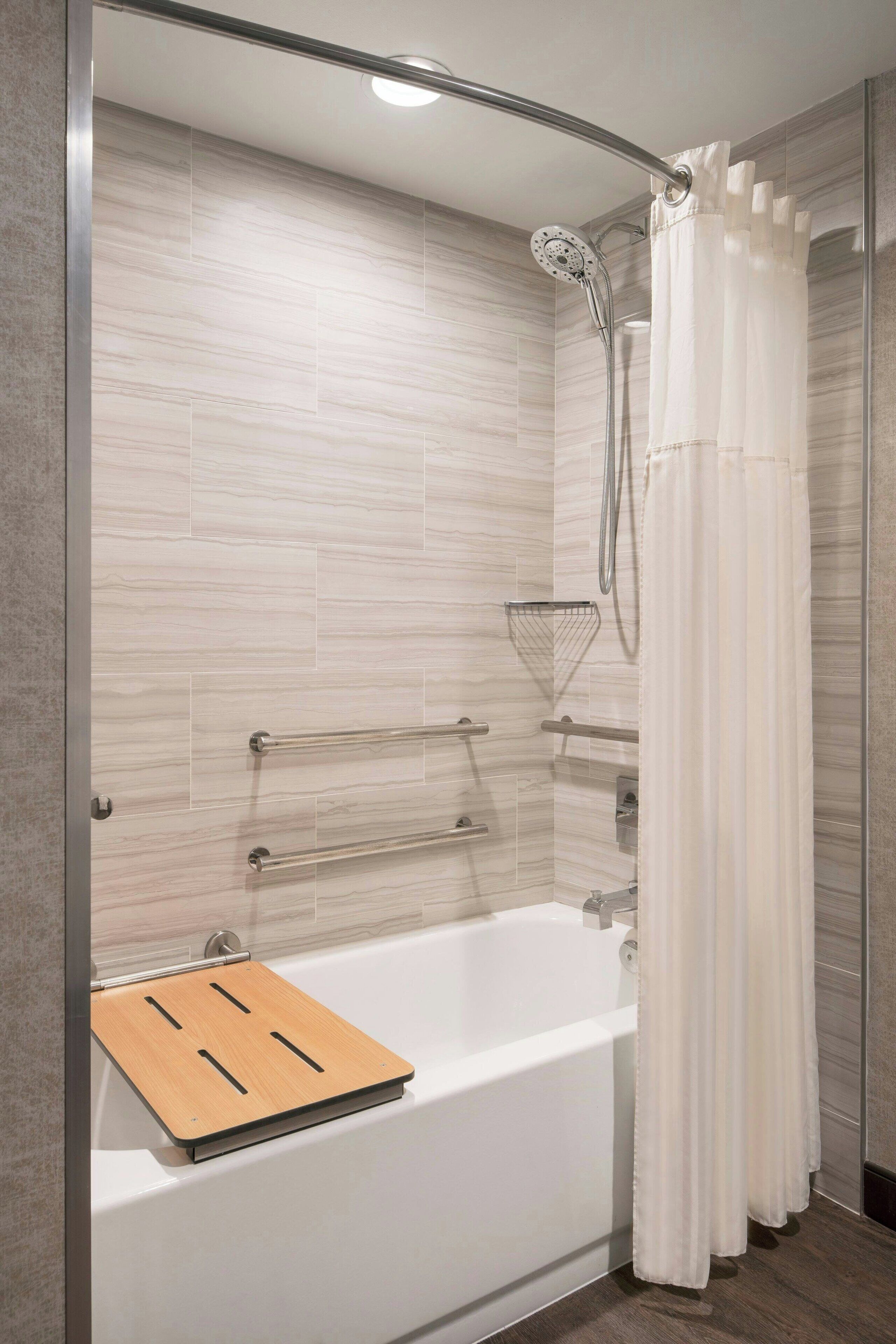 A modern bathroom with a shower, a bathtub, and a wooden bath mat.