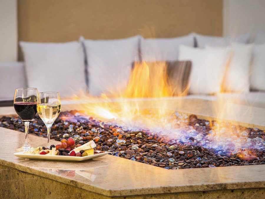 A fire feature with a stone surround, two glasses of wine, and a plate of fruit.