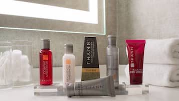 Une salle de bain contenant divers produits de toilette, notamment un flacon de shampoing rouge, un savon blanc, un gel douche gris et un tube de lotion rose.