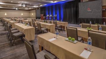 A conference room with multiple tables, chairs, and a stage with a screen.
