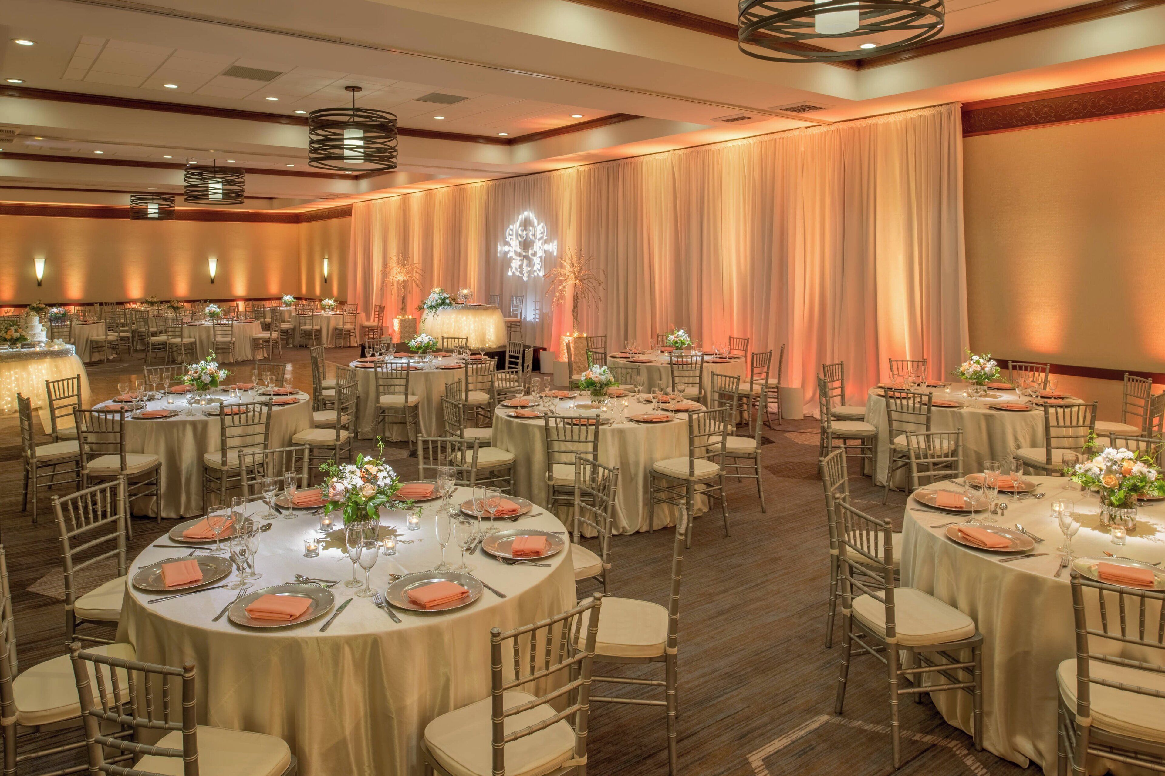 Une salle de banquet avec des tables rondes, des chaises et un grand écran de projection.