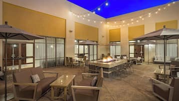An outdoor patio area with seating, a central fire feature, and string lights.