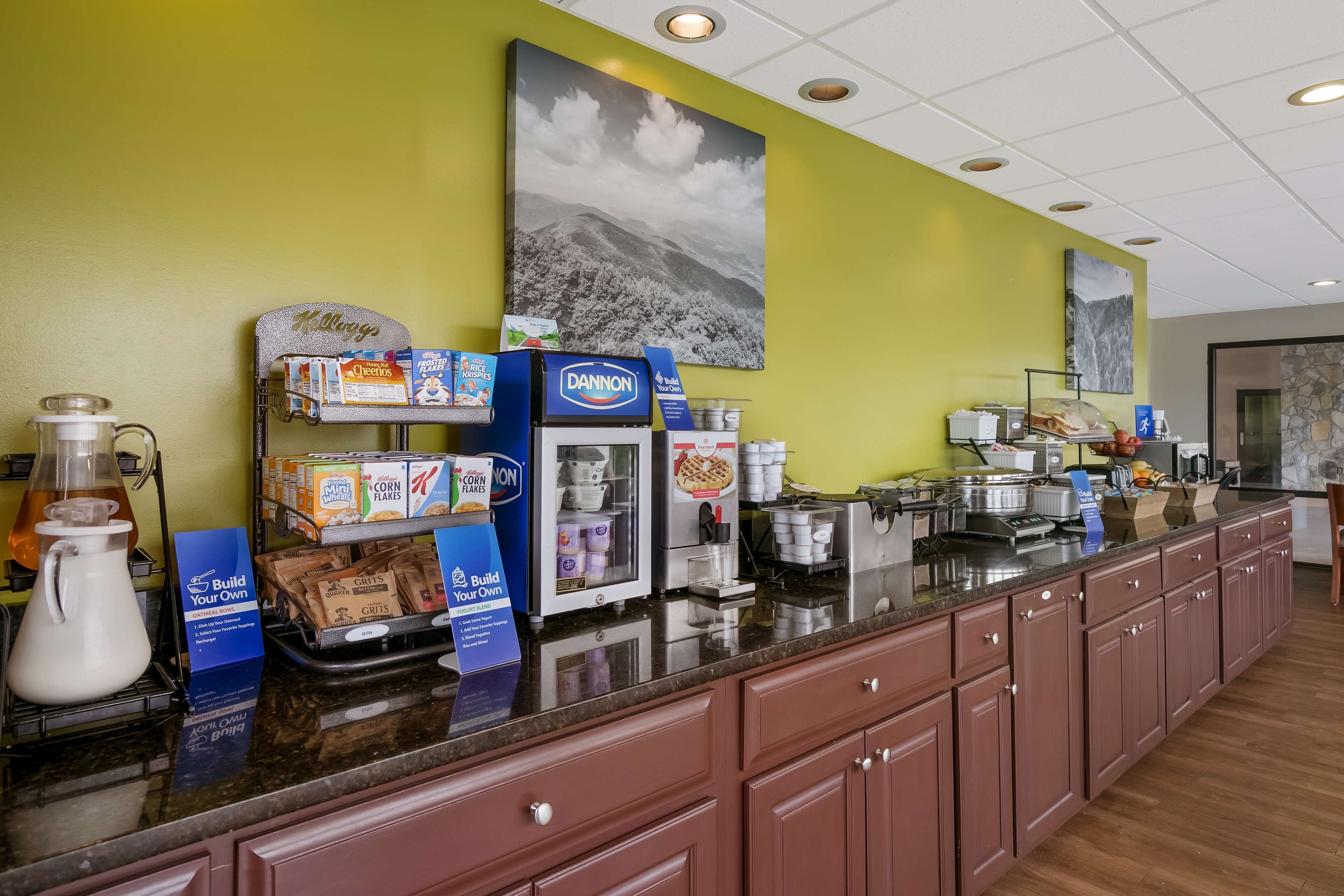 A breakfast bar with various food items, a coffee machine, and a sign promoting a breakfast program.