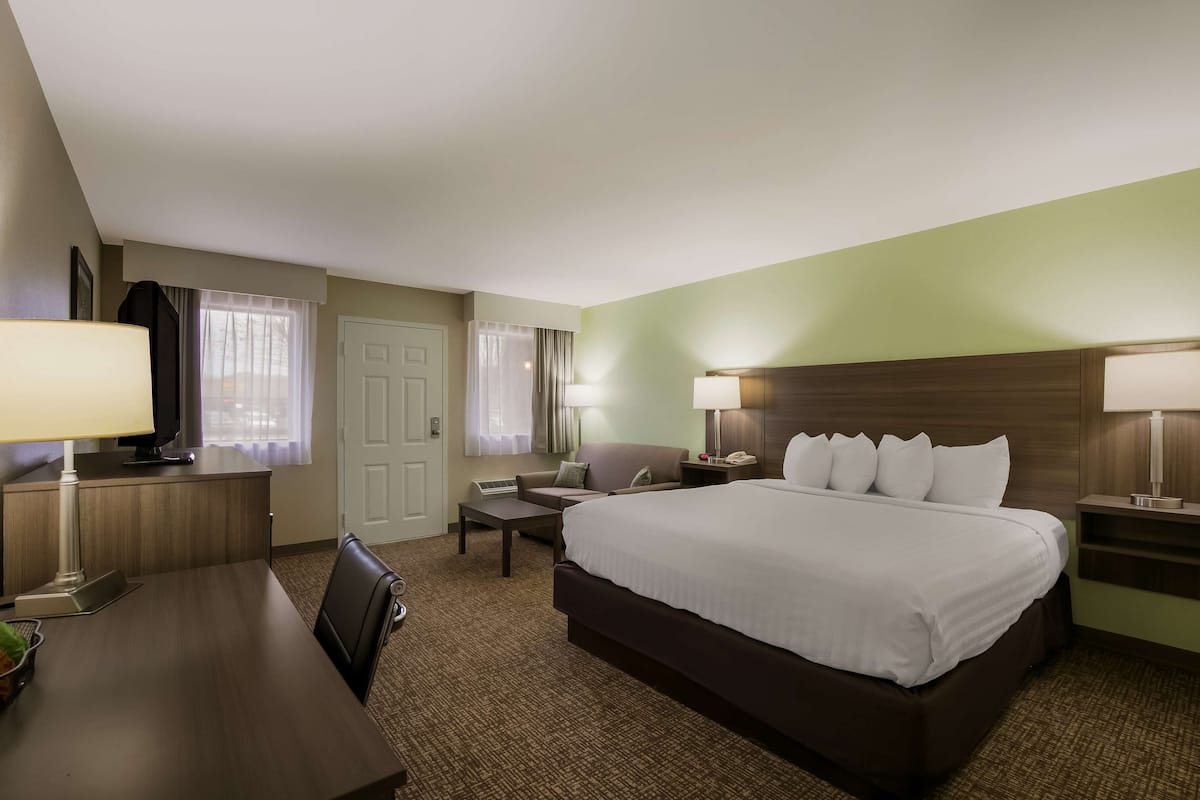 A hotel room with a large bed, a desk with a lamp, a chair, a TV, and a window with curtains.
