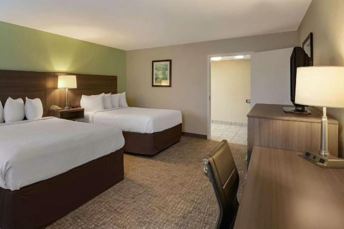 A hotel room with two beds, a desk, a chair, a lamp, and a television.