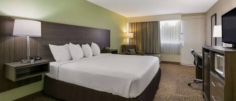 A hotel room with a large bed, a desk, a chair, a TV, and a window with curtains.