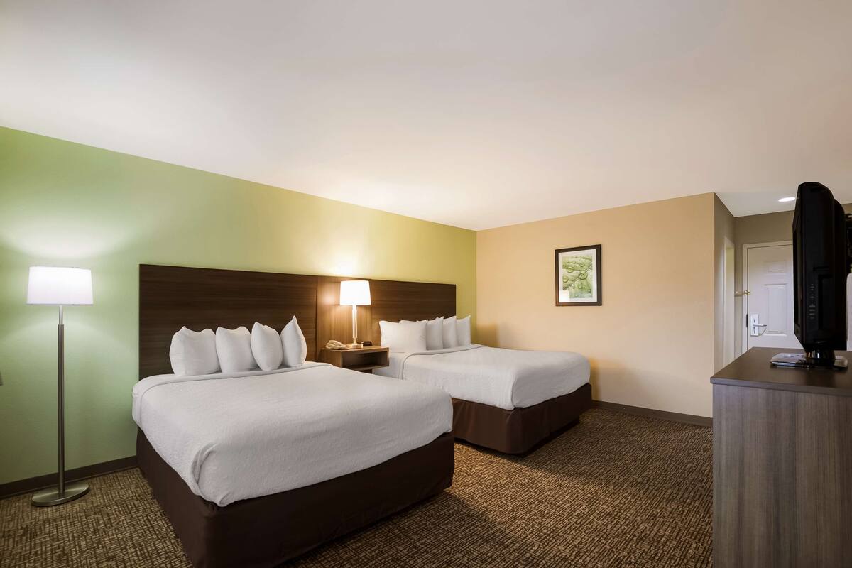 A hotel room with two beds, a desk, a lamp, and a television.