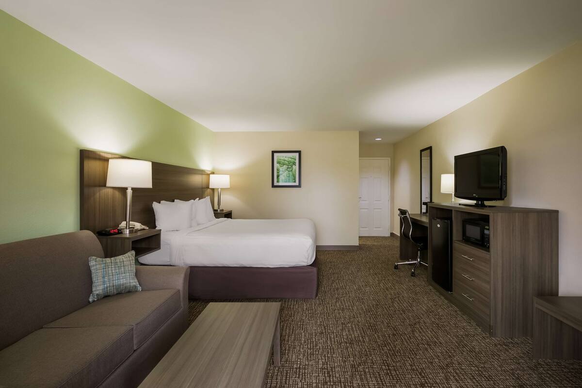 A hotel room with a bed, a sofa, a desk with a computer, a TV, and a lamp.