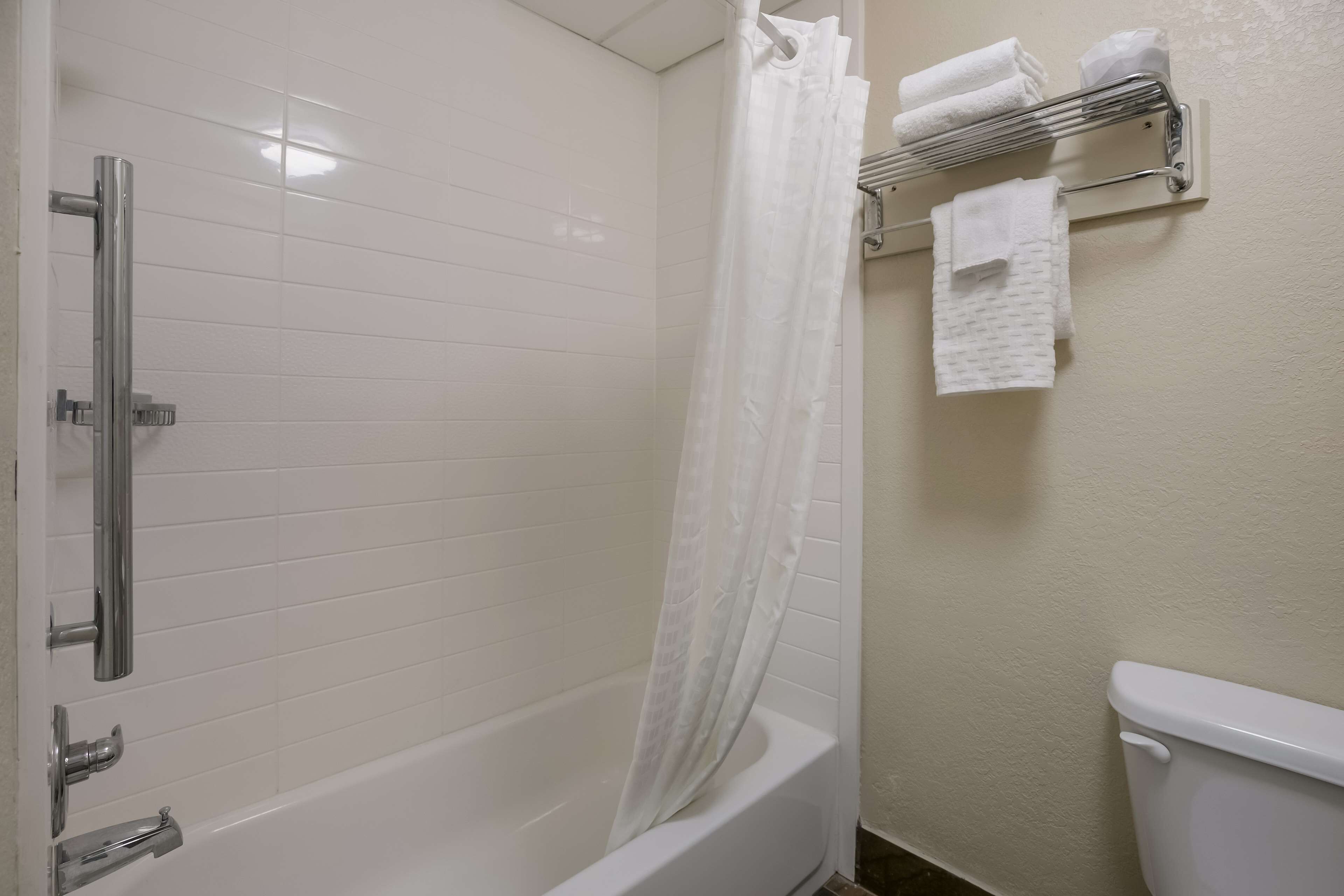 A bathroom with a bathtub, a shower curtain, a towel rack with towels, and a toilet.