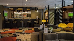 A bar area with multiple seating options, a patterned carpet, and a television screen.