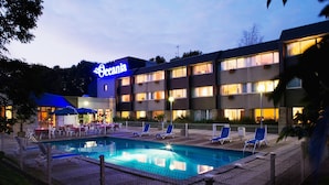 A hotel with a swimming pool, outdoor seating, and a neon sign.