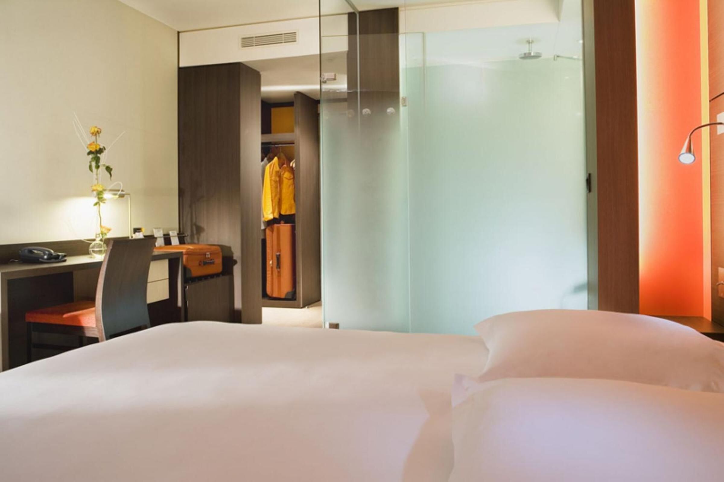 Una habitación de hotel con una cama, un escritorio con una silla, un teléfono y un florero con flores.