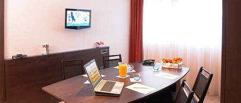 A conference room with a laptop, a glass of orange juice, and a fruit basket on the table.