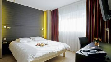 Una habitación de hotel con una cama, un escritorio con un teléfono y un jarrón de flores, y una ventana con cortinas.