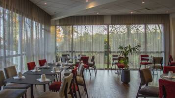 Une salle de conférence équipée de tables et de chaises, de grandes fenêtres et d’une plante en pot.