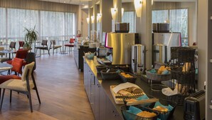 A hotel breakfast area with seating, a buffet counter, and a coffee machine.