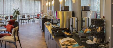A hotel breakfast area with seating, a buffet counter, and a coffee machine.