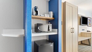 Une chambre d’hôtel moderne équipée d’un four à micro-ondes, d’un réfrigérateur, d’une machine à café et d’un téléviseur posé sur un meuble.