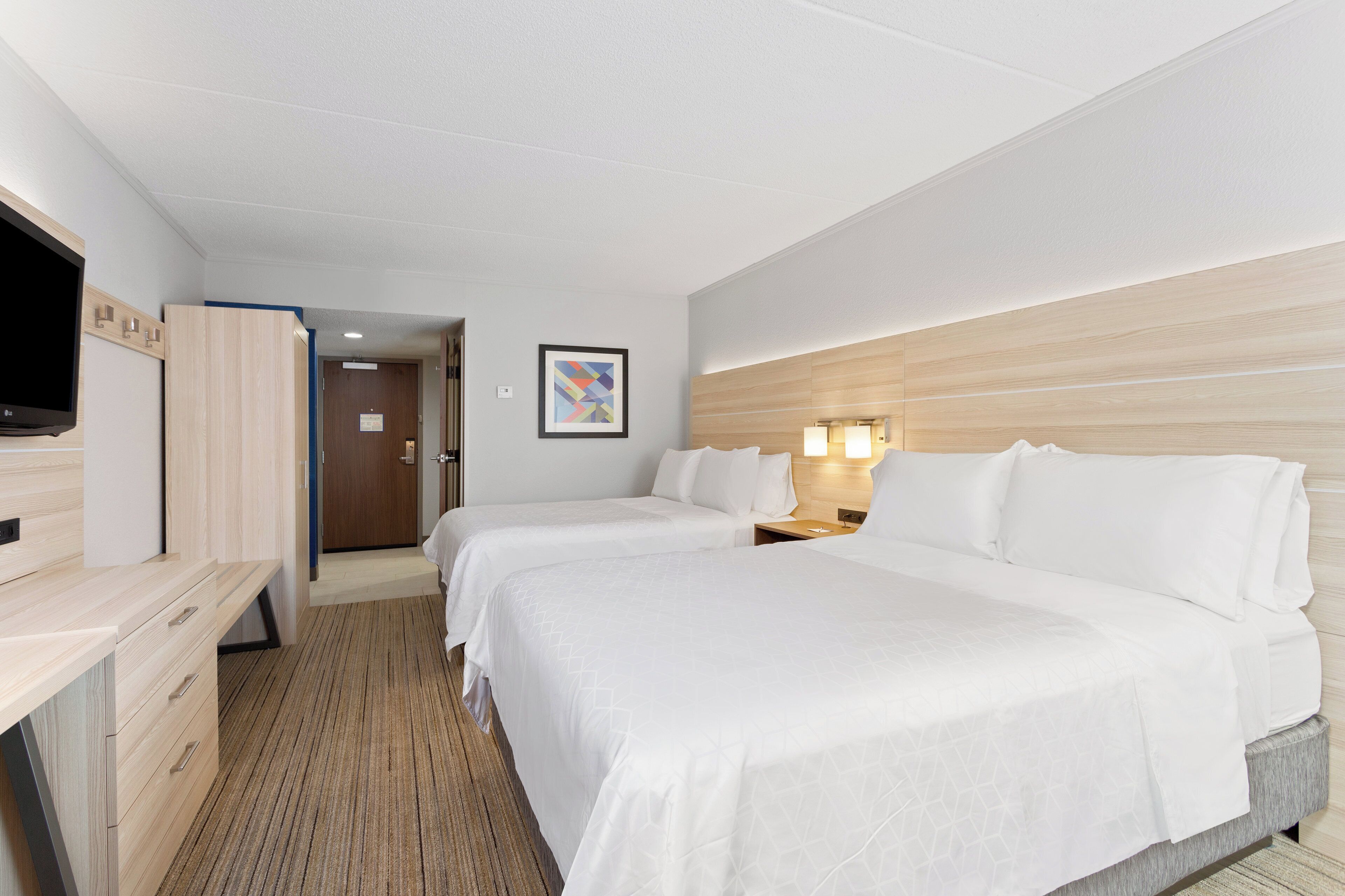 A hotel room with two beds, a desk, a TV, and a door leading to another room.