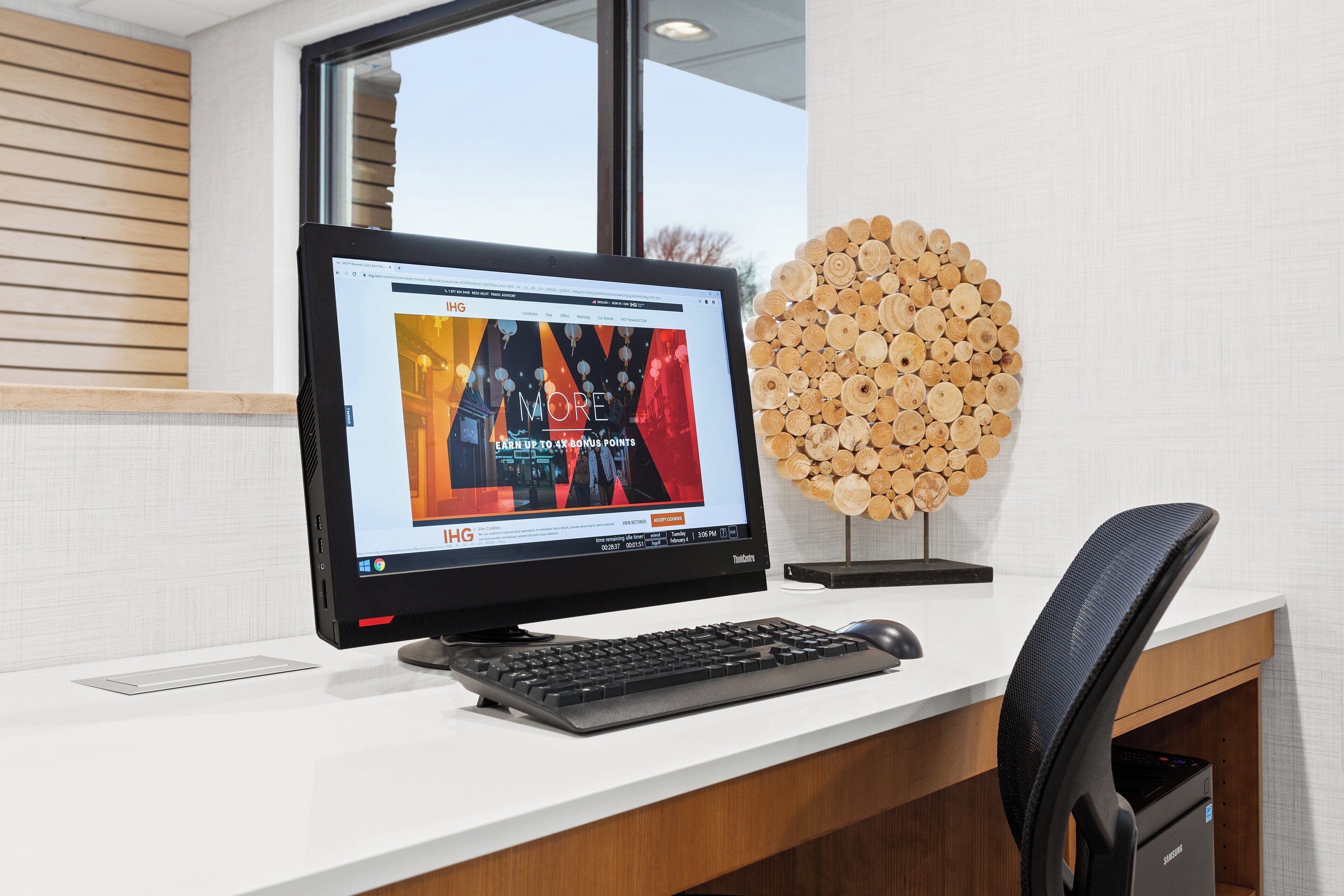 Een modern bureau met een computer monitor, toetsenbord en muis. Op het bureau staat een decoratieve houten blokhut.