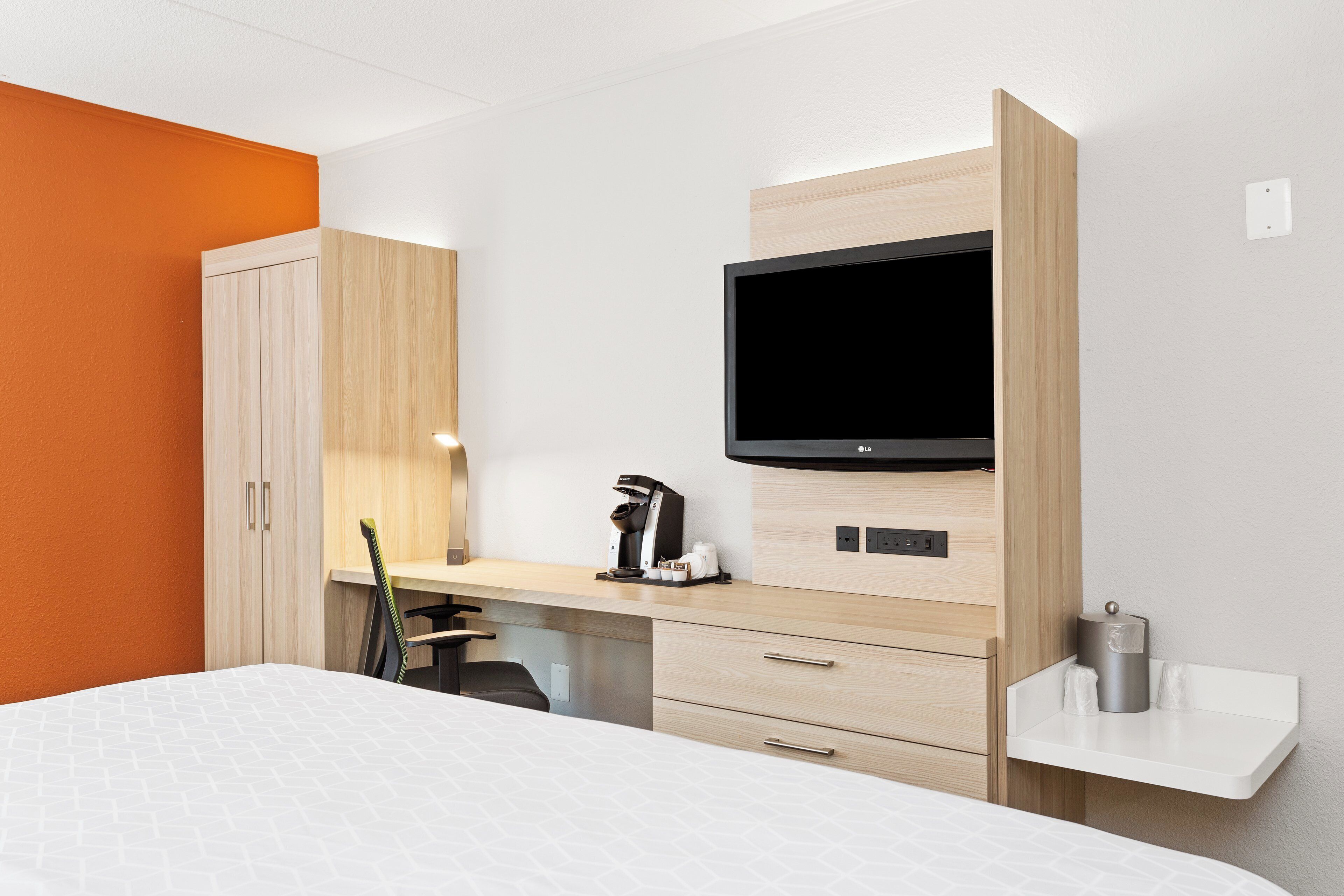 A hotel room with a bed, a desk with a coffee maker, a TV, and a wardrobe.