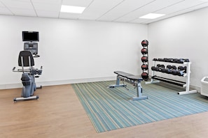 Une salle de sport équipée de matériel d’exercice, notamment un tapis de course, un banc de musculation et des haltères.