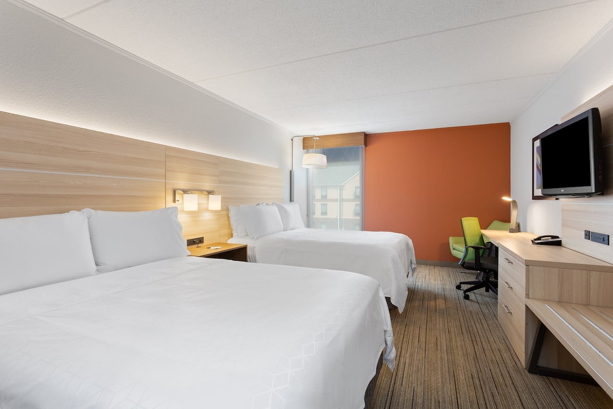 Ett hotellrum med två sängar, ett skrivbord, en stol, en tv och ett fönster.
