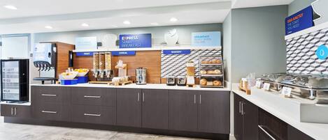 A breakfast area with a self-serve station, including a yogurt dispenser, cereal, and bakery items.