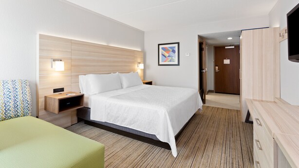 Une chambre d’hôtel comprenant un lit, des tables de chevet, un téléviseur et une porte donnant sur un couloir.