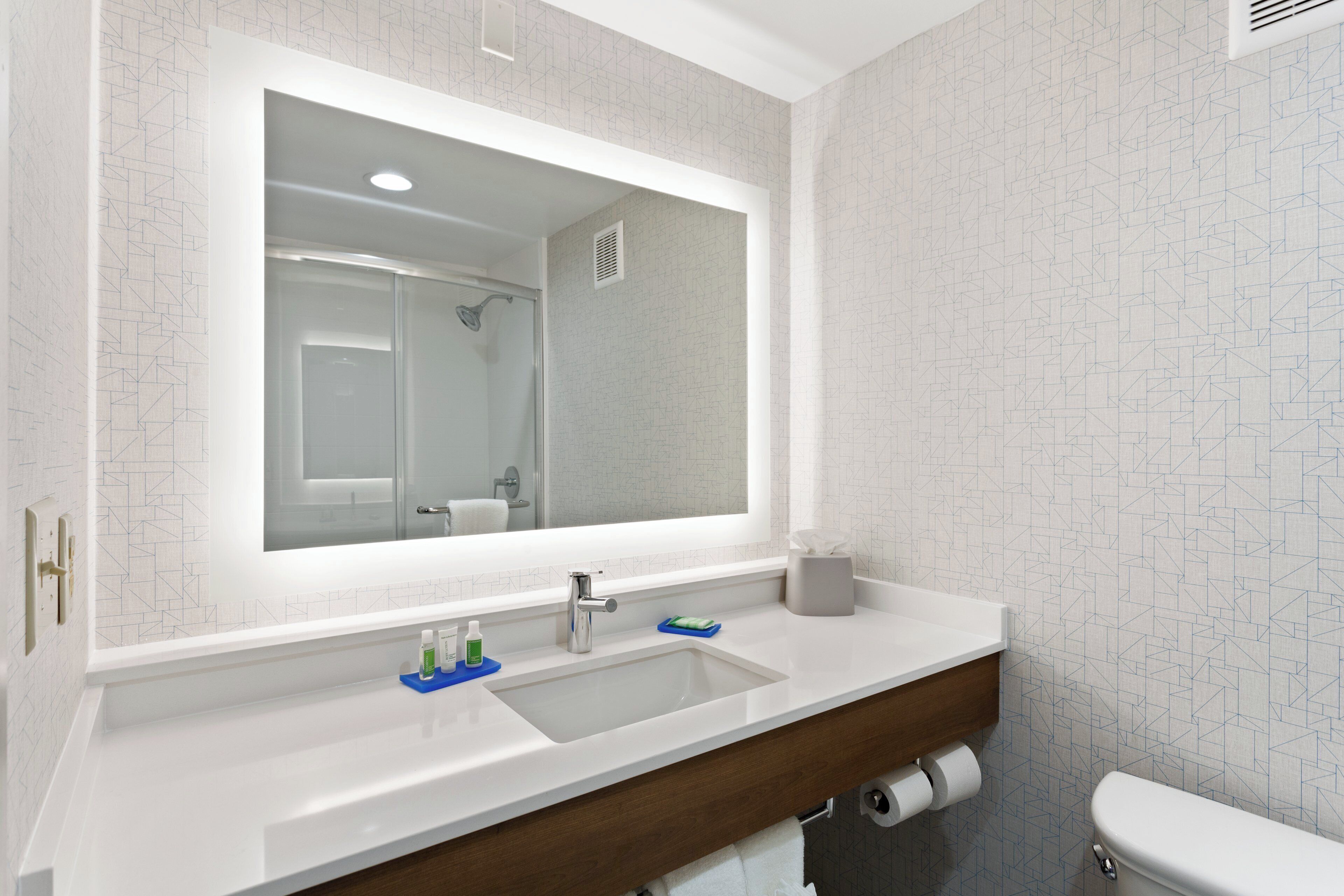 A modern bathroom with a large mirror, a sink, and a toilet.