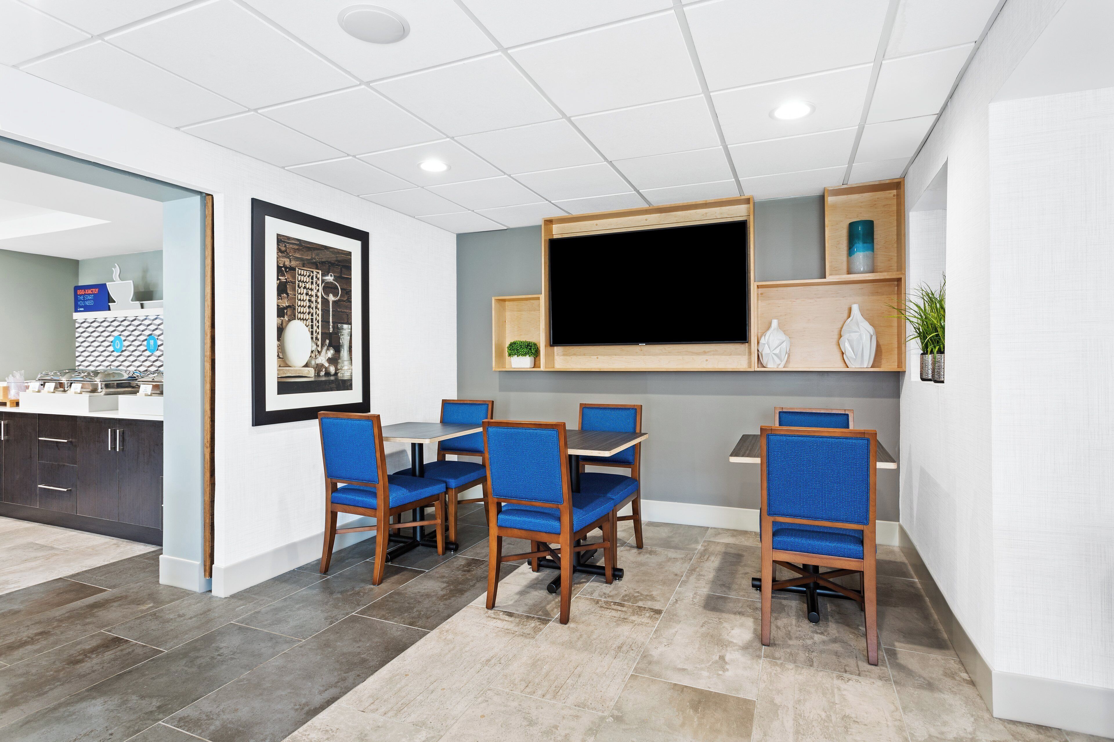 A modern dining area with a large TV, wooden chairs, and a framed picture on the wall.